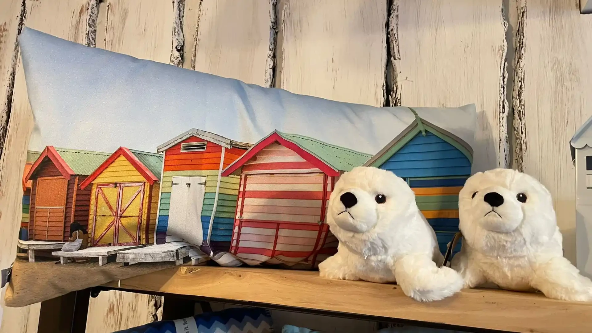 Langes Kissen mit bunten Strandhütten und zwei Plüsch-Robben auf Holzregal